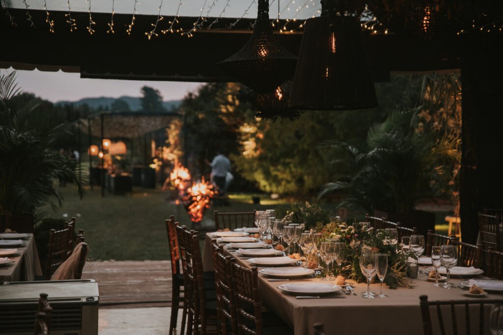 Table with plates, cutlery, glasses, flowers and candles with wooden chairs. Wedding decoration.